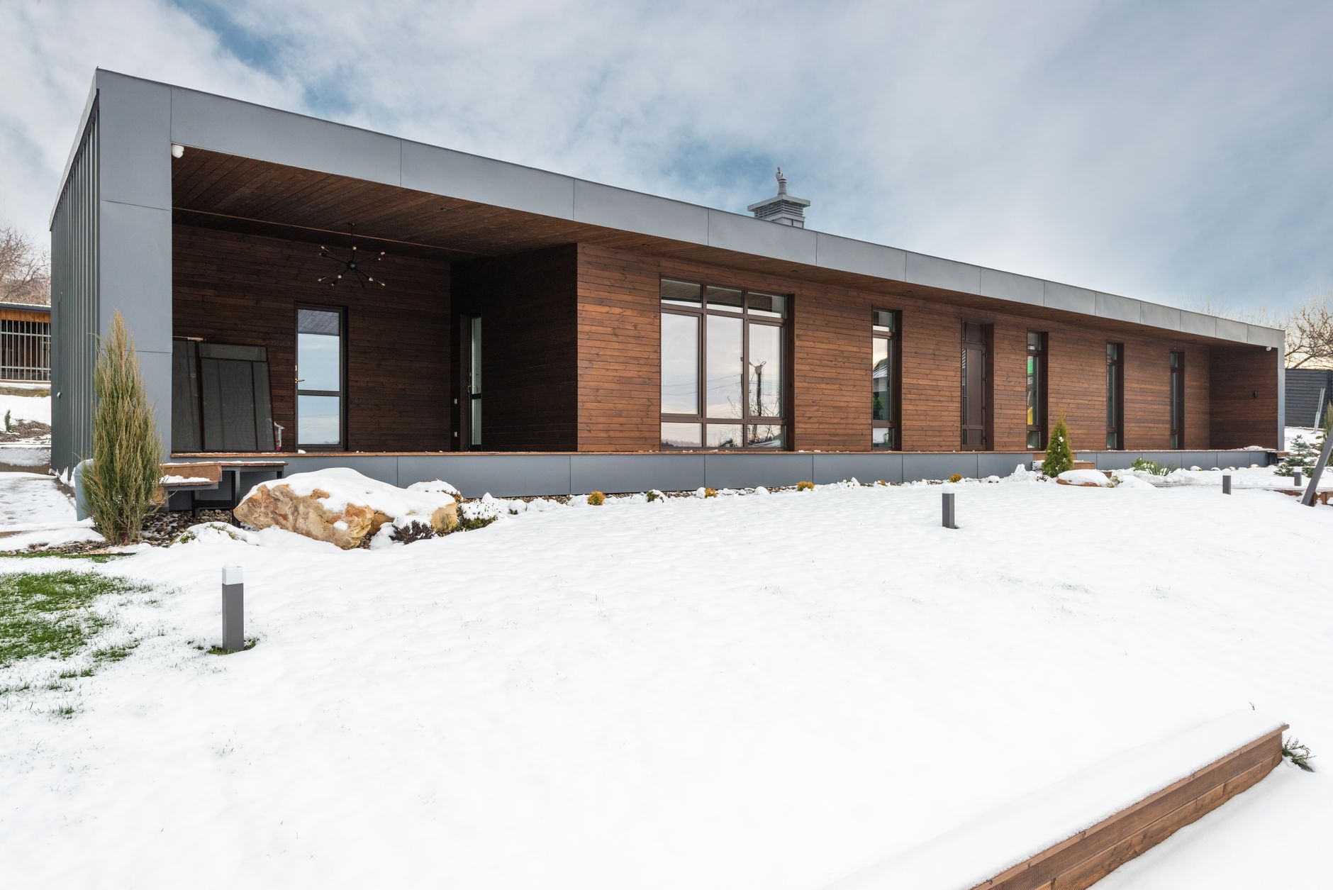 A sleek modern wooden house stands surrounded by a snowy winter landscape, showcasing contemporary architecture.